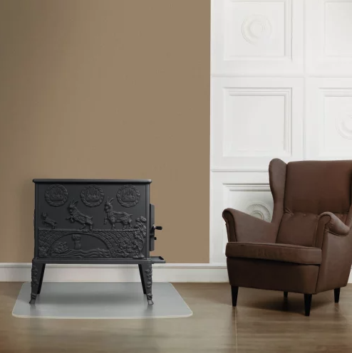 Schwarzer Kaminofen aus Gusseisen mit Tiermotiv vor einem Sessel.